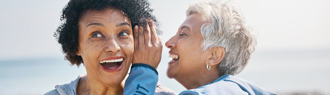 Two older women are whispering into each other 's ears.