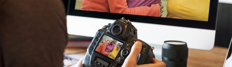 A person is holding a camera in front of a computer screen.