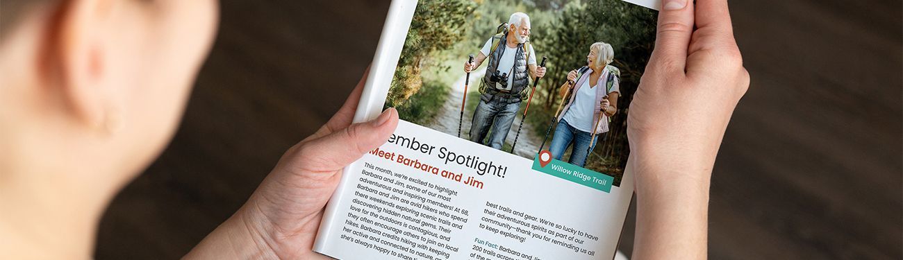 A person is holding a newsletter with a picture of two people hiking on it.