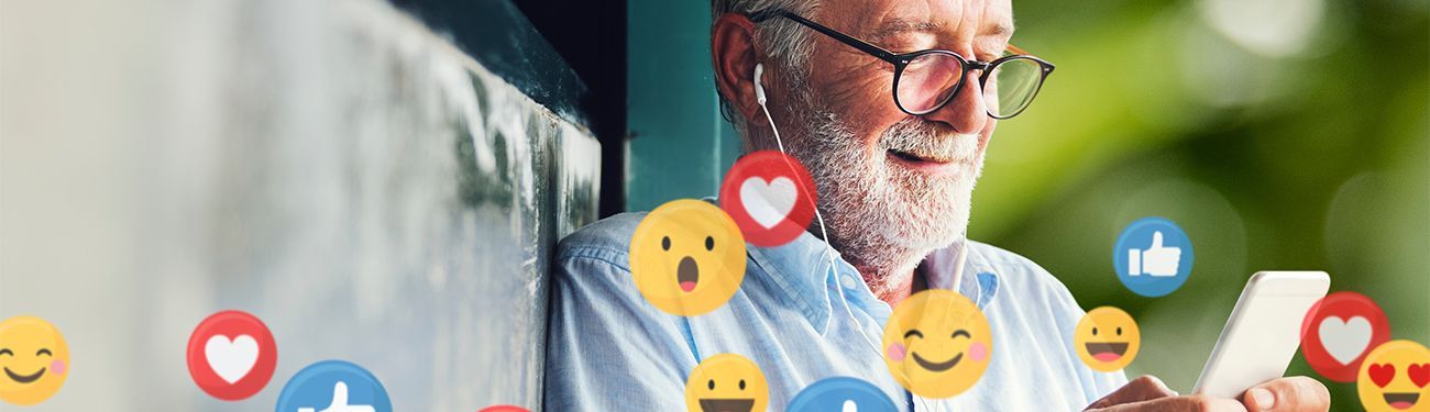 An elderly man is using a cell phone with smiley faces coming out of it.