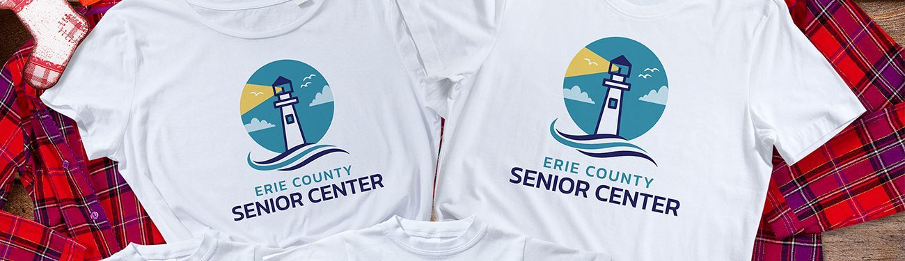 Two white t-shirts with a lighthouse on them are sitting on top of a plaid blanket.