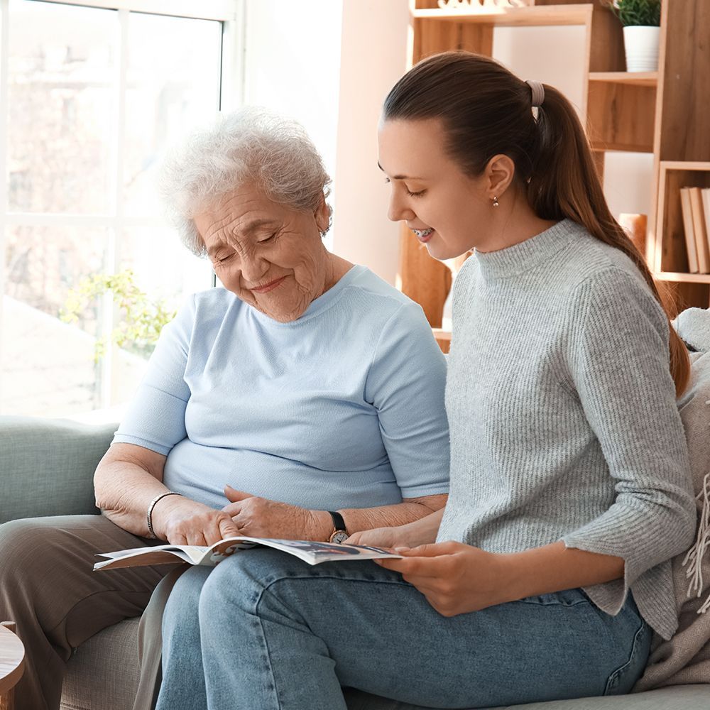 Two women sitting on a couch reading a newsletter, smiling. 