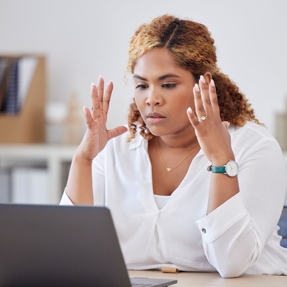 Woman with hands raised in front of laptop, looking stressed.
