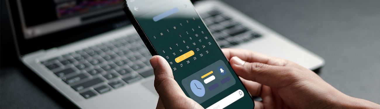 A person is holding a cell phone in front of a laptop.