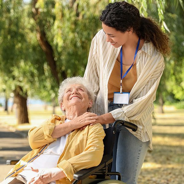 A woman is standing next to an elderly woman in a wheelchair.