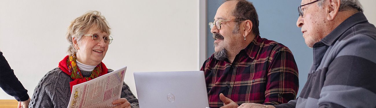 A group of older adults are sitting around a table looking at a newsletter.