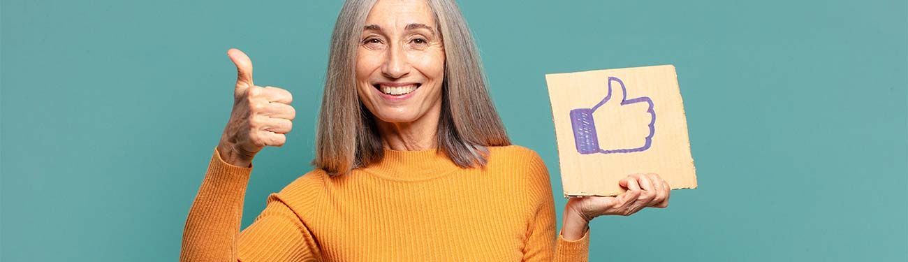 A woman is holding a cardboard sign with a thumbs up sign drawn on it.
