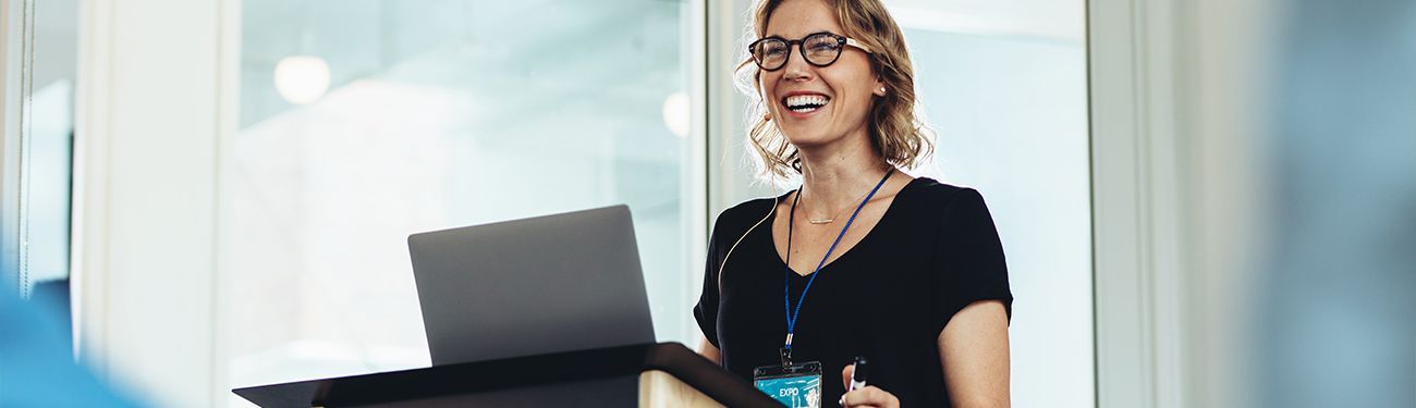 A woman is standing in front of a window holding a laptop computer.