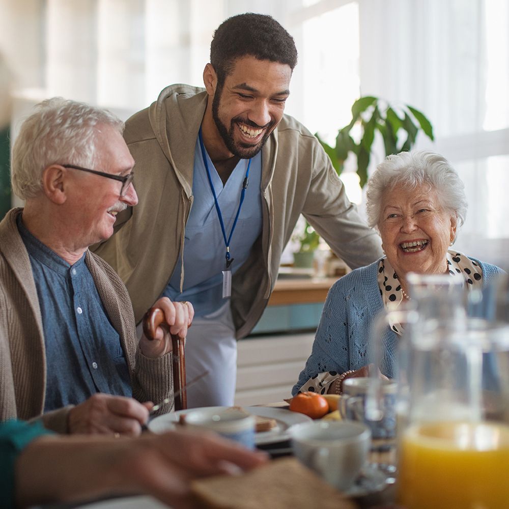 Group of elderly people and a caregiver smiling together indoors.