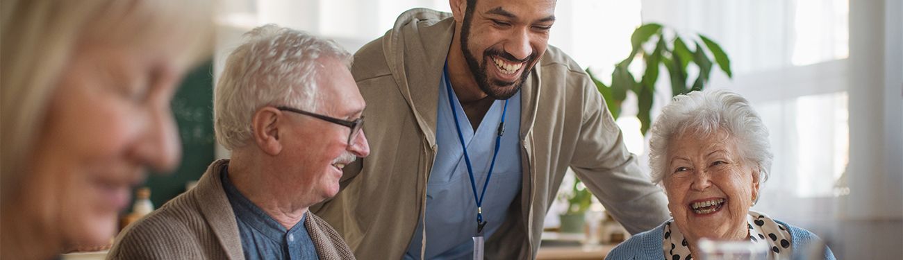 Group of elderly people and a caregiver smiling together indoors.