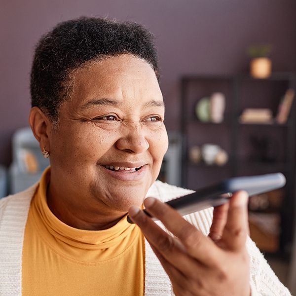A woman is smiling while holding a cell phone in her hand.