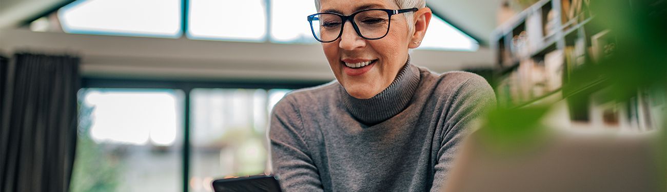 A woman wearing glasses is smiling while using a laptop computer.