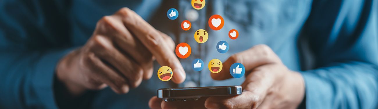 A man is holding a cell phone with social media icons coming out of it.