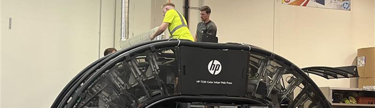 A man in a yellow shirt is standing next to a black hp computer.