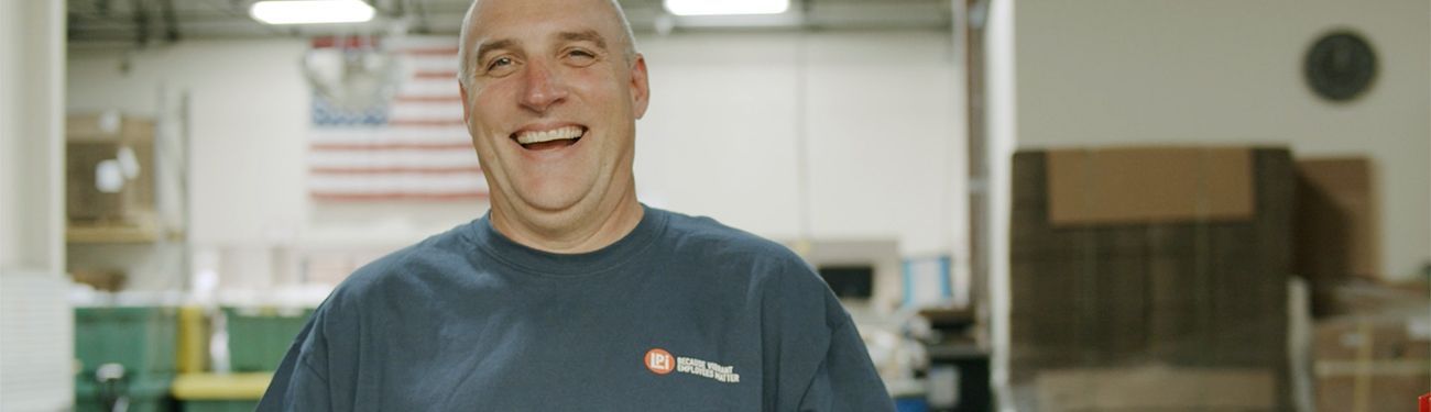 A man in a blue shirt is smiling in a factory.