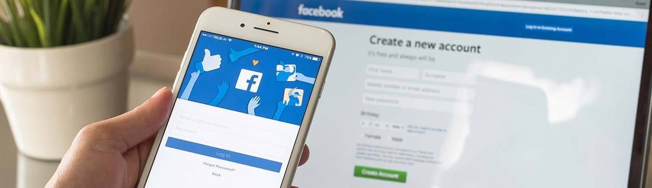 A person is holding a cell phone in front of a laptop.