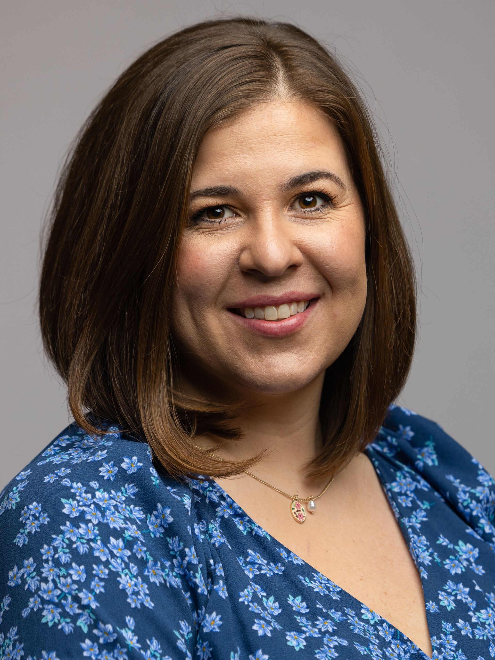 A woman in a blue floral dress is smiling for the camera.
