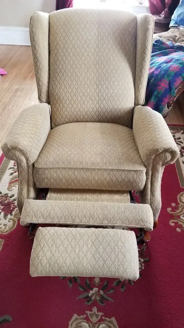 A cozy beige recliner with a diamond pattern sits on a red floral carpet. 