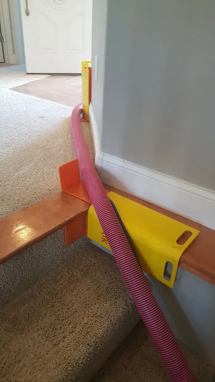 A pink vacuum hose is creatively threaded through bright yellow knee boards to prevent door frame damage.
