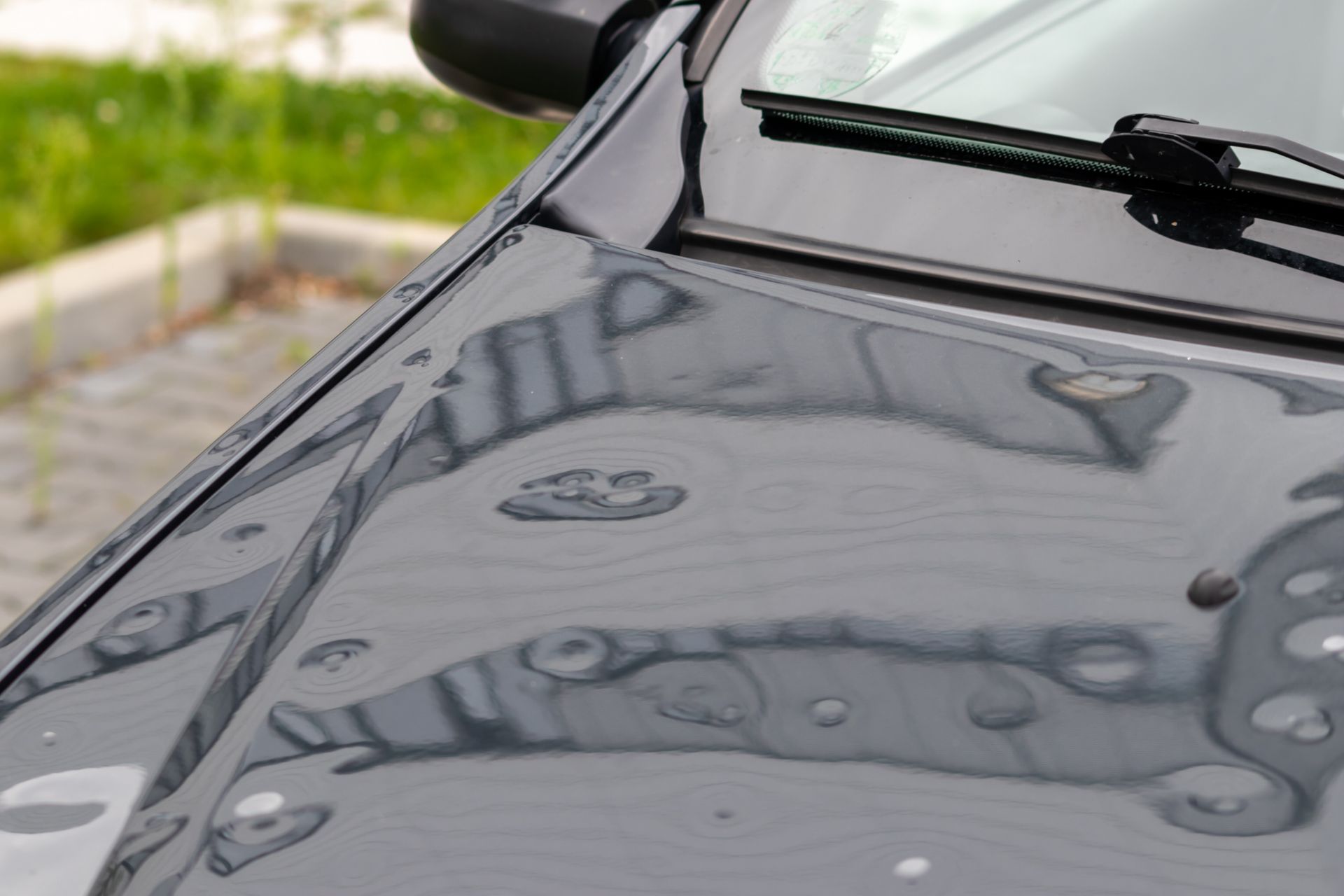 Close-up of a dark grey car hood damaged by hail, showing numerous dents and reflections.