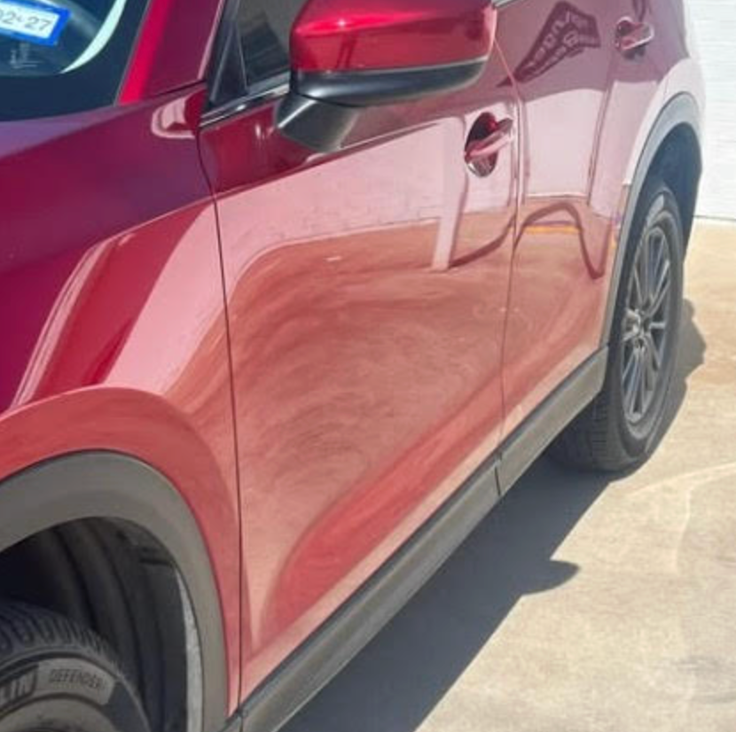 The side profile of a red SUV, showing the front and rear passenger doors, side mirror, and dark alloy wheels.