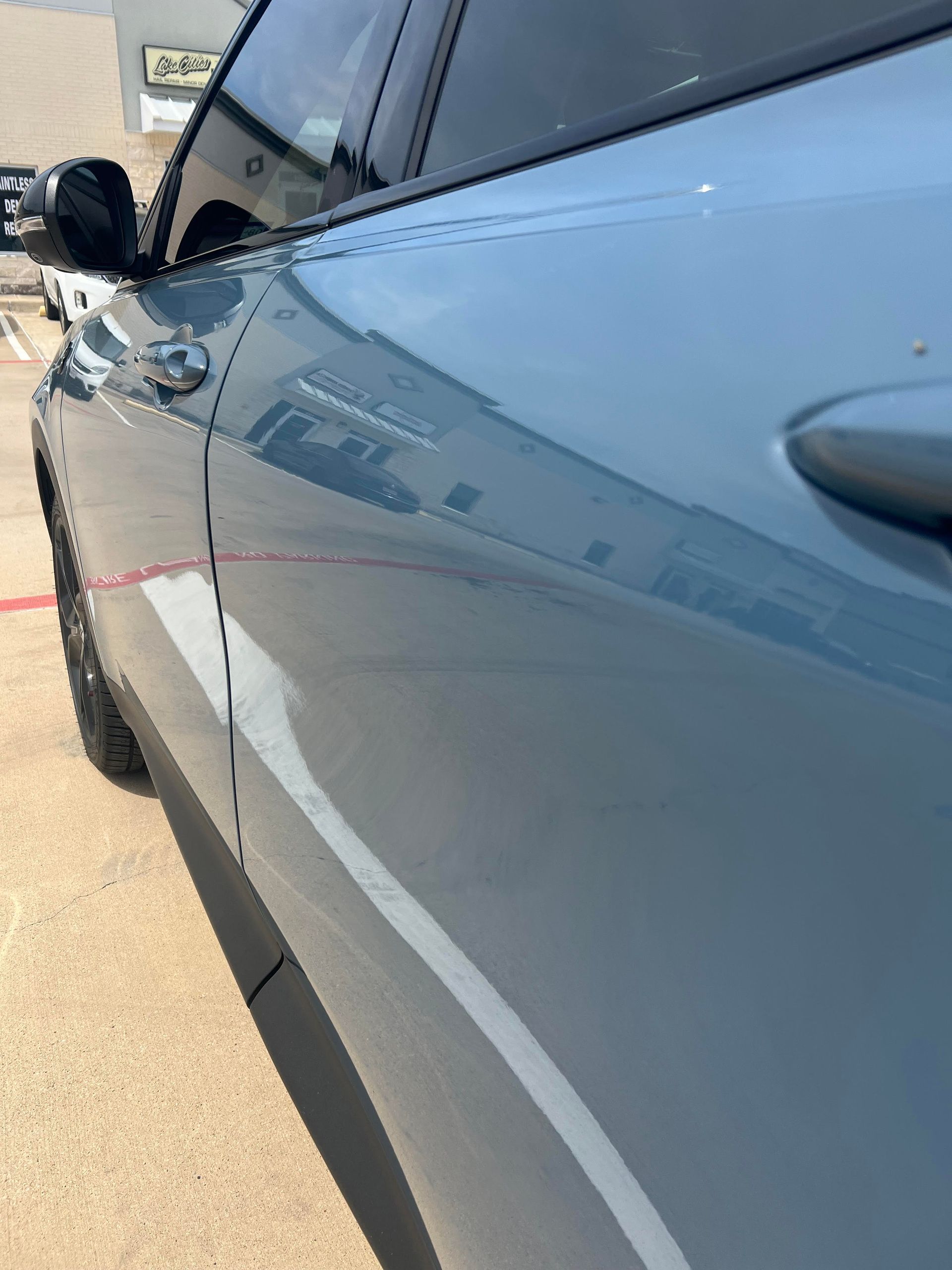A side view of a glossy, light blue car parked outdoors on concrete pavement.