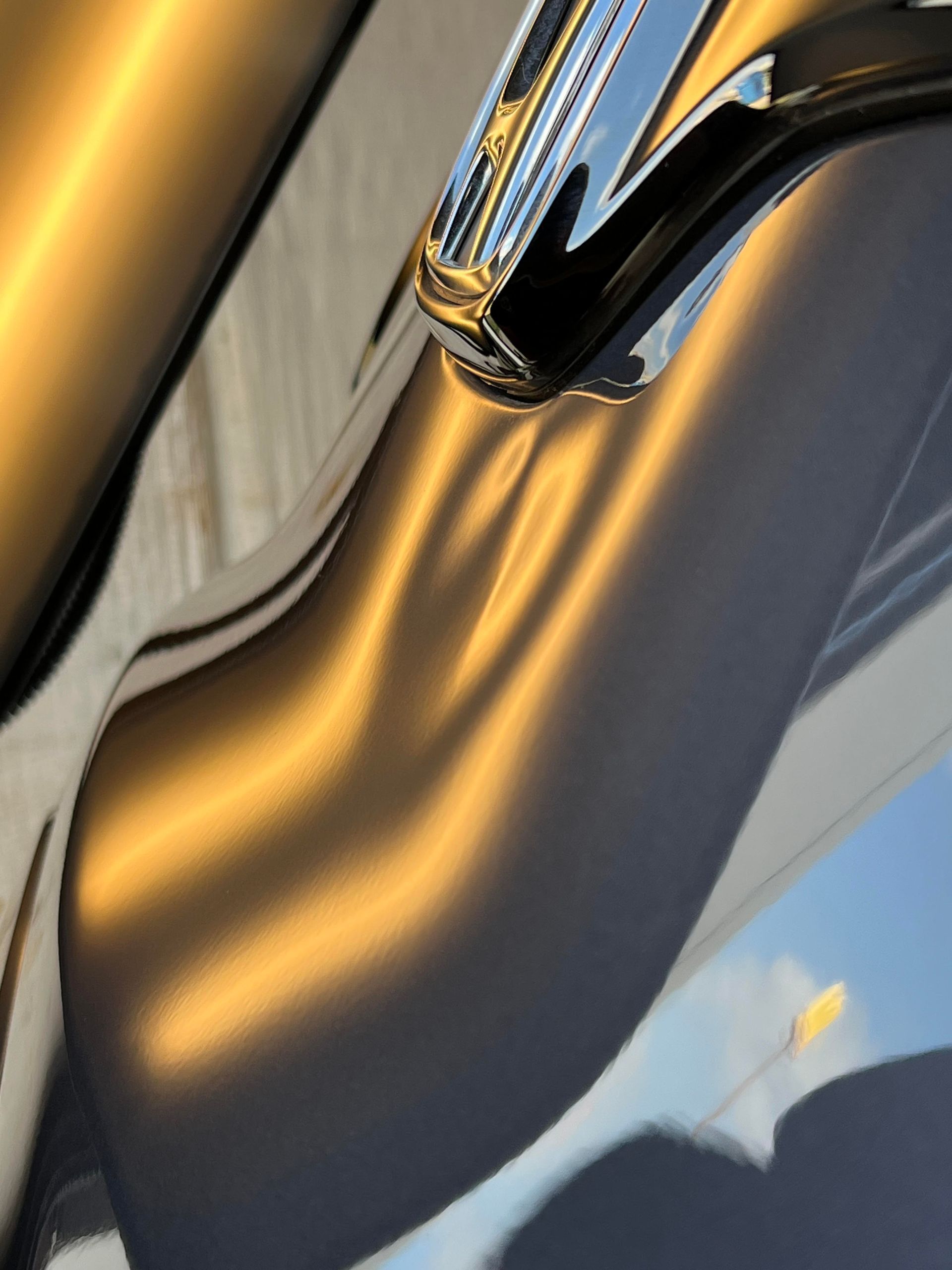 Close-up of a deep dent on a dark vehicle’s body panel, showing distorted reflections of sunlight and a chrome trim.