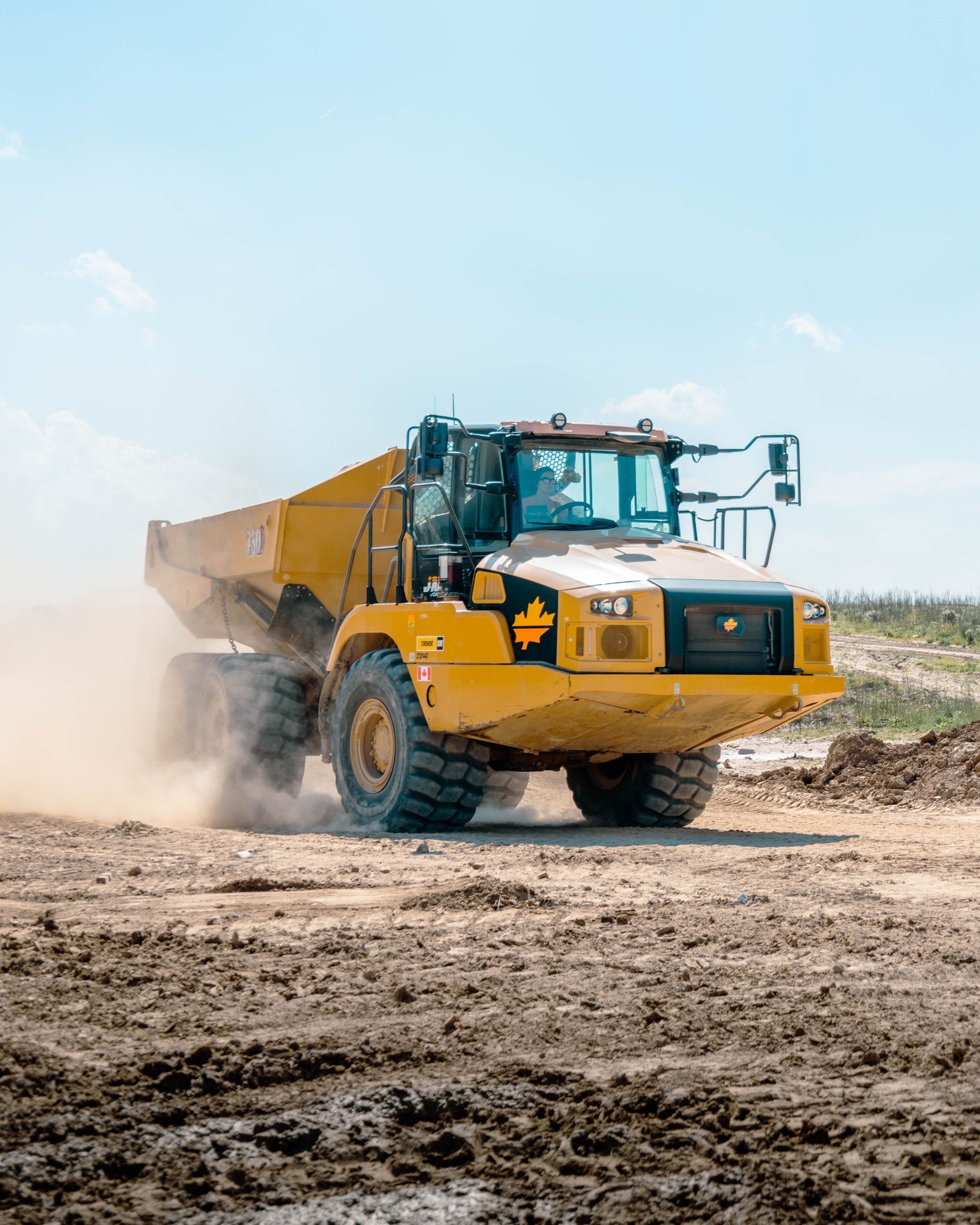 A yellow dump truck is driving through a muddy field.