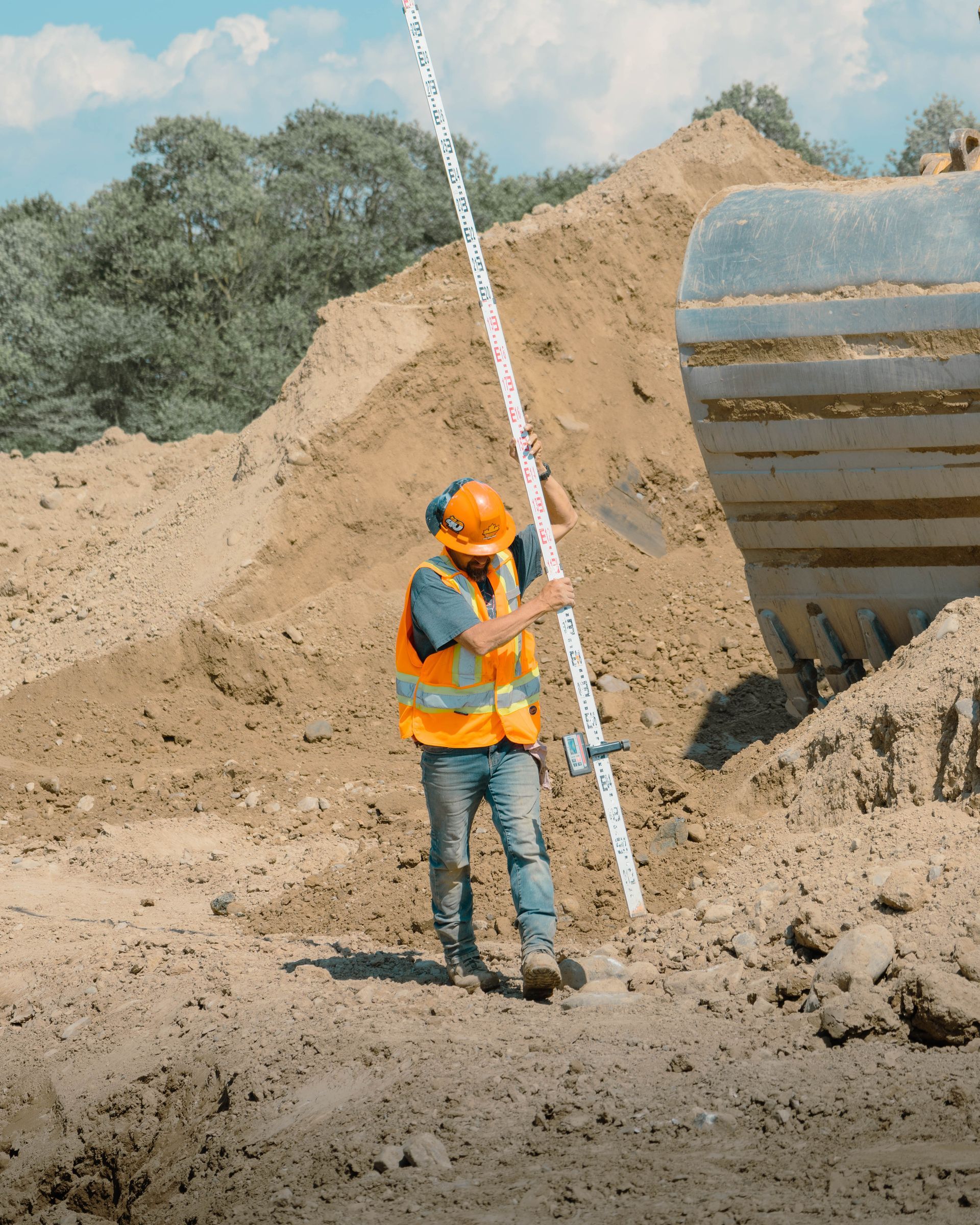 A construction worker is standing in the dirt holding a pole.