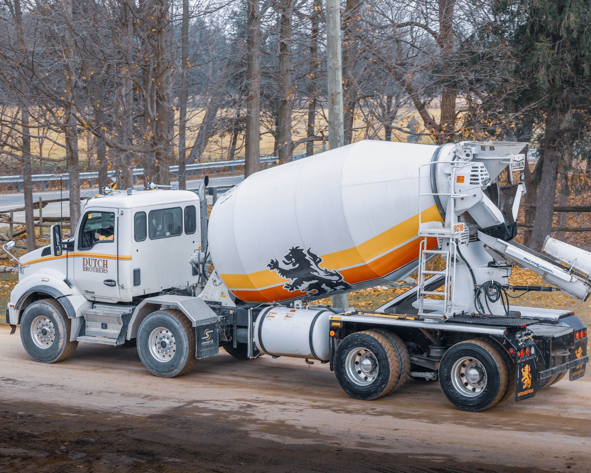 A concrete mixer truck is driving down a dirt road.