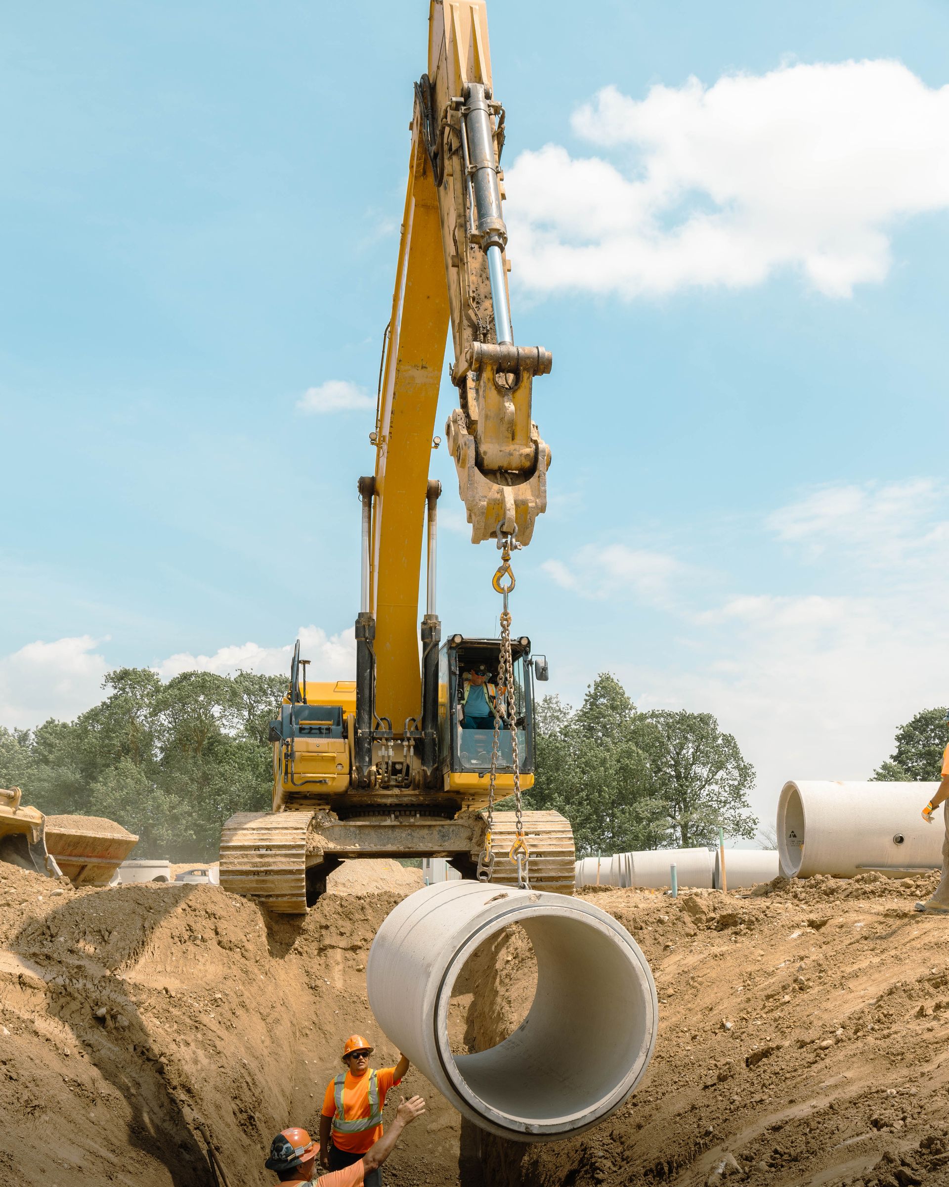 A construction site with a yellow excavator lifting a large pipe.