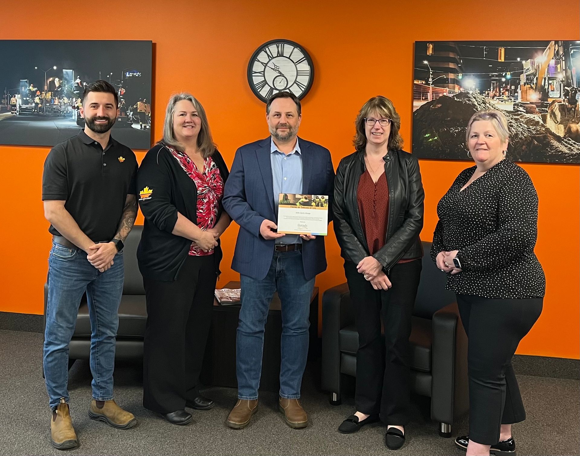 A group of people are standing in front of an orange wall holding a certificate.