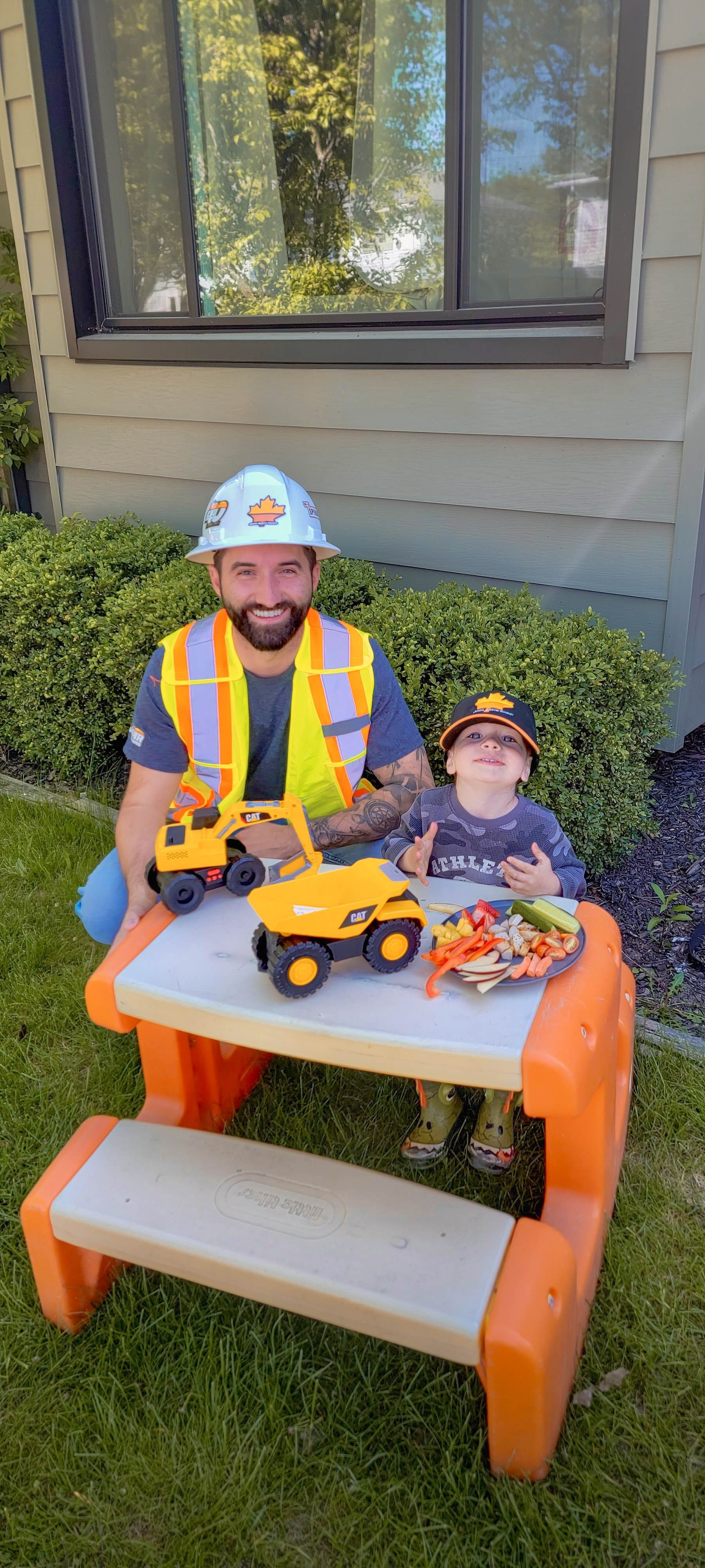 a man and a child are sitting at a picnic table with toy trucks .