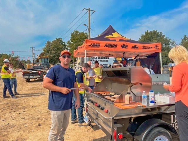 a group of people are standing around a grill on a trailer .
