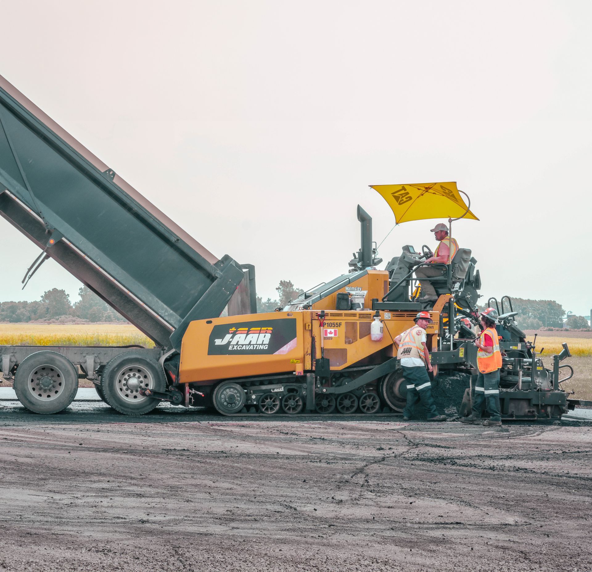 a yellow and black asphalt paver is being loaded onto a dump truck .