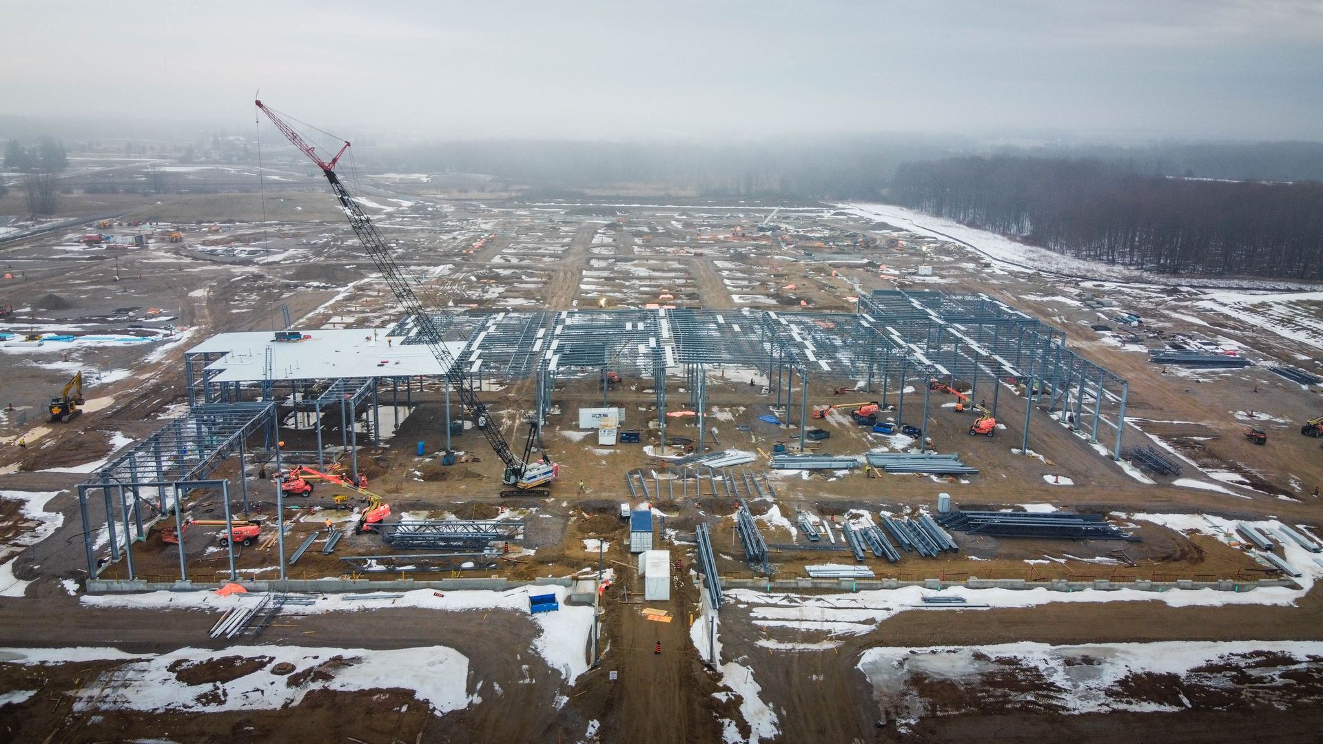An aerial view of a large building under construction in the middle of a snowy field.