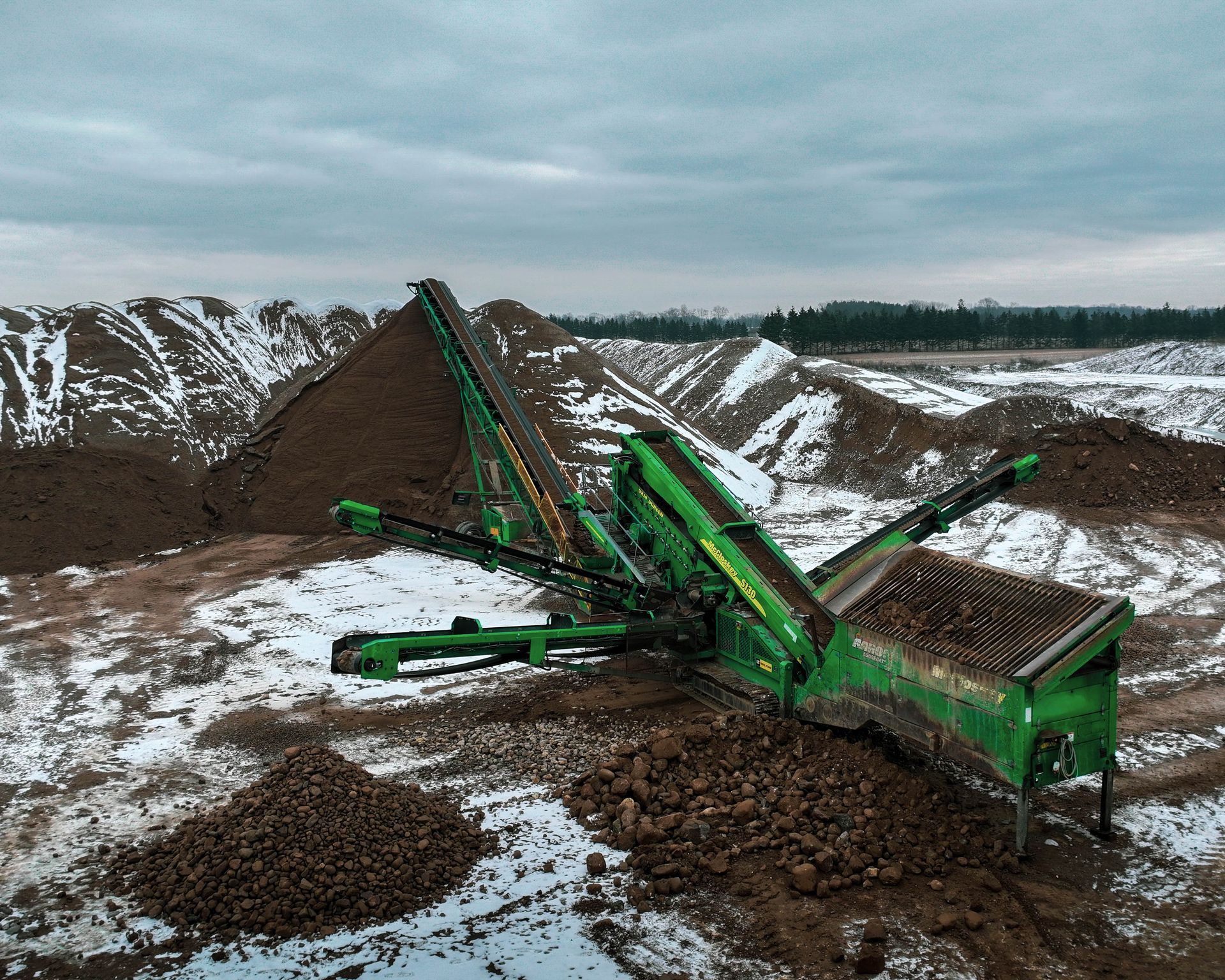 a green machine is sitting on top of a pile of dirt .