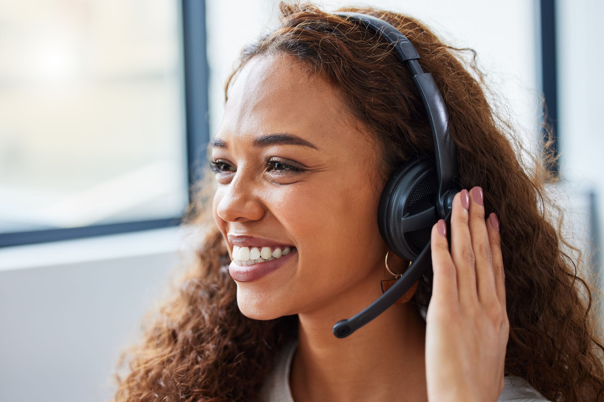 A woman is wearing a headset and smiling while talking on a phone.