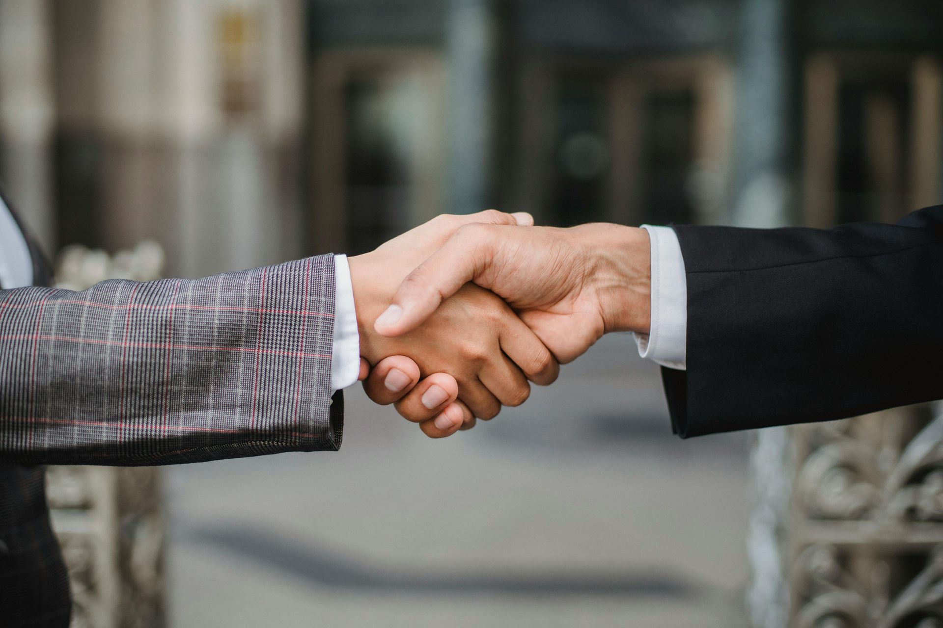 Two people shaking hands, likely in a business setting, near a building entrance.