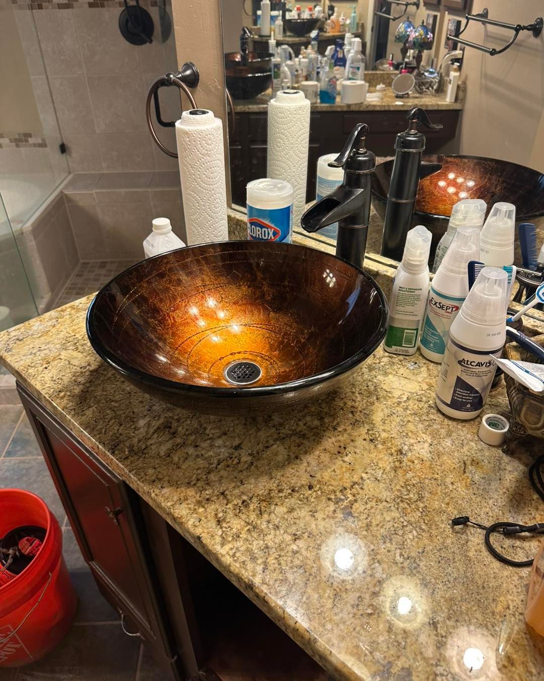 A brown and orange glass vessel sink on a granite countertop in a bathroom.