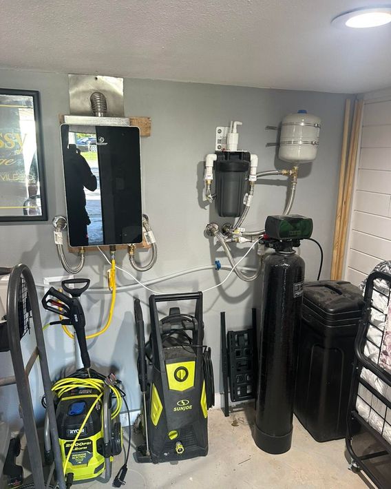 Water heater and filtration system in a utility room; black, silver, and white equipment on a gray wall.