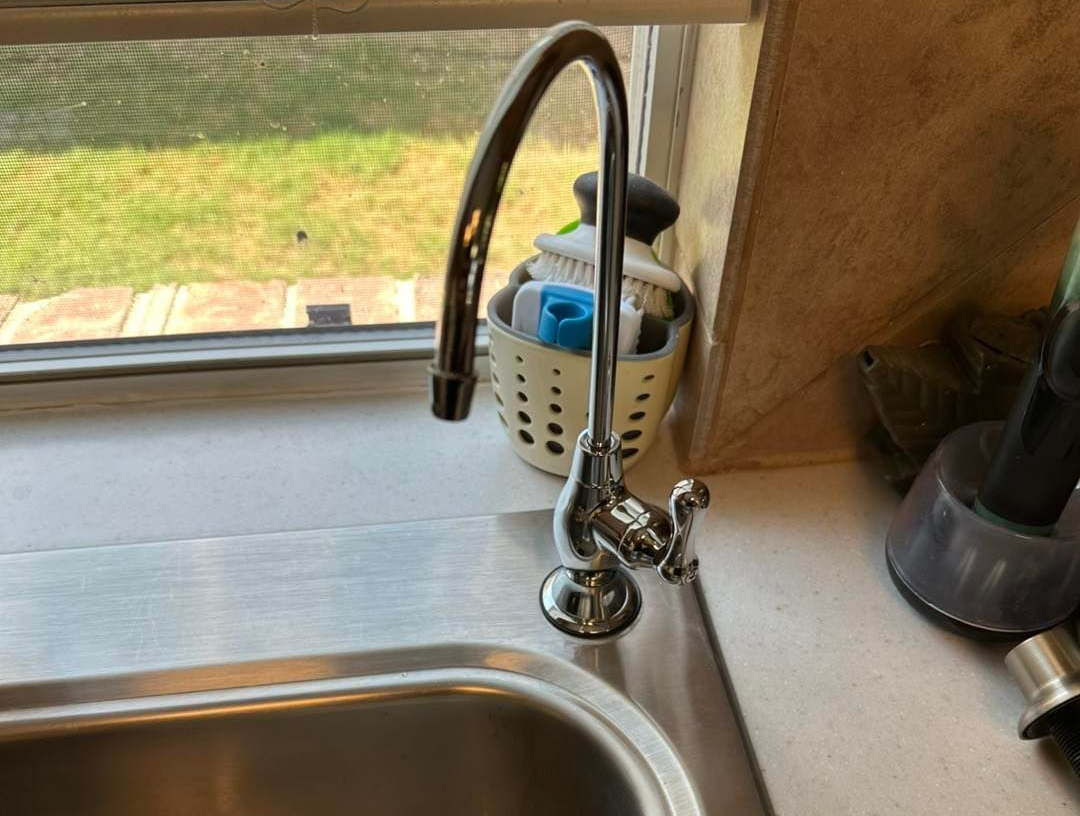 Stainless steel sink with chrome faucet, next to a window overlooking greenery.