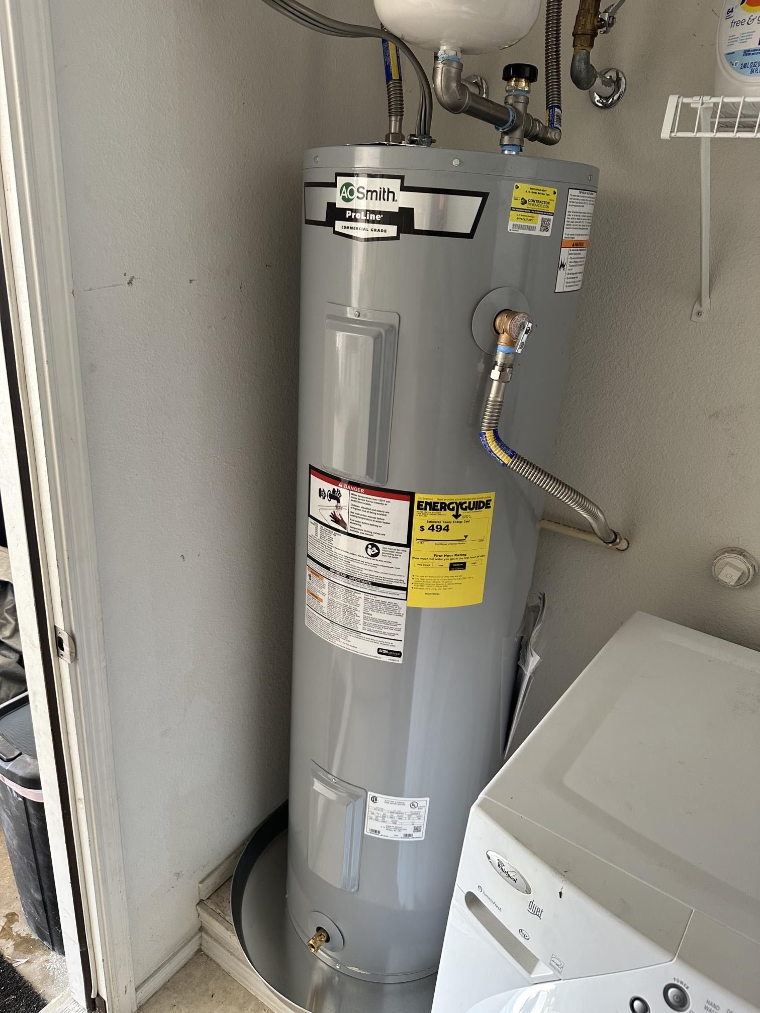 Gray water heater in an outdoor utility room next to a white washing machine.