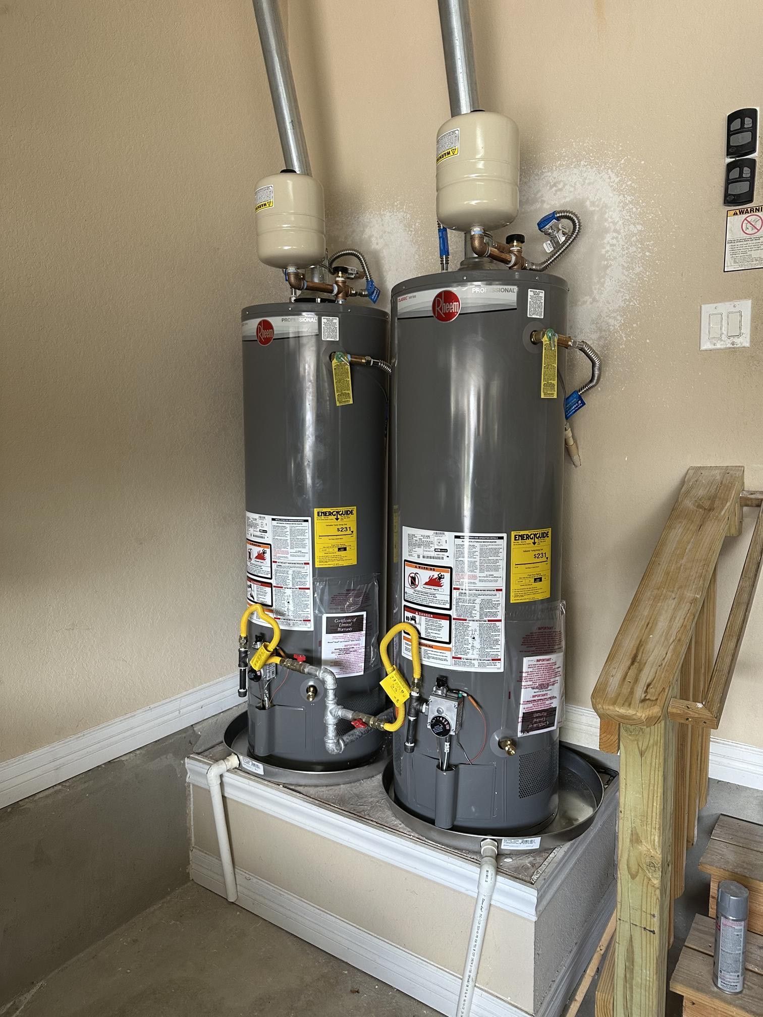 Two gray Rheem water heaters side-by-side on a raised platform, in a garage.