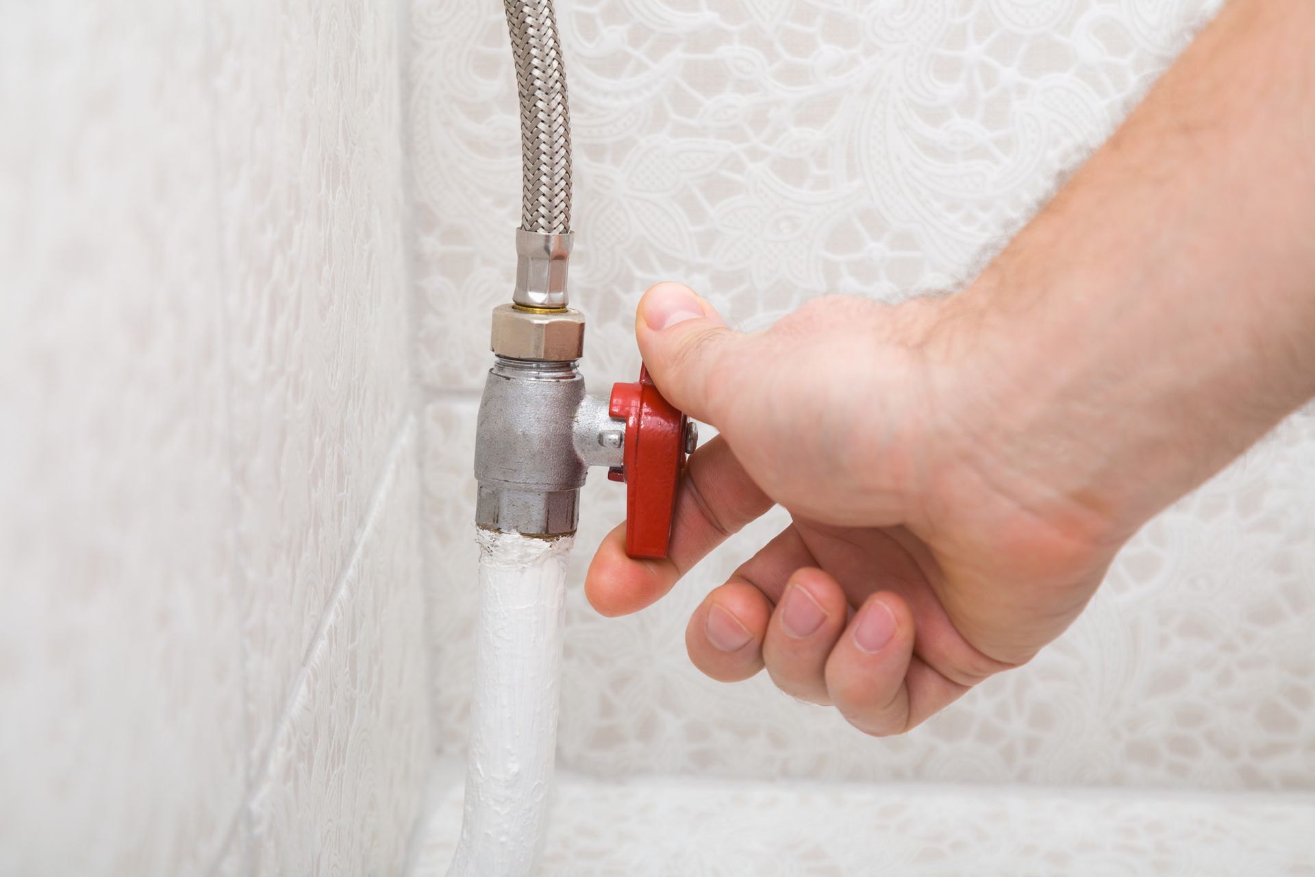 Hand turning a red valve, stopping water flow from a flexible hose connected to a wall.