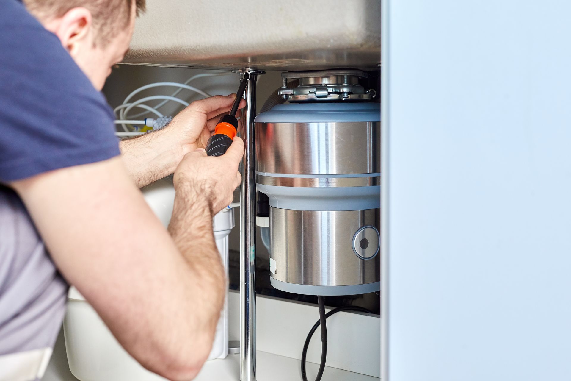 Man installing a garbage disposal under a kitchen sink, using a screwdriver.