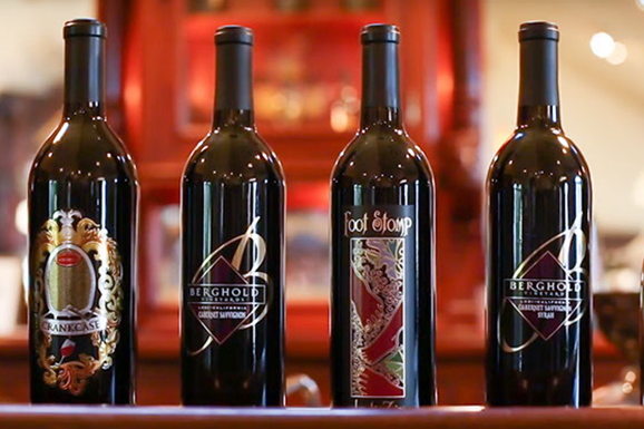 Four bottles of red wine are lined up on a shelf