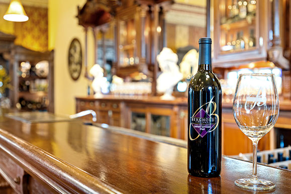 A bottle of wine is sitting on a wooden bar next to a wine glass.