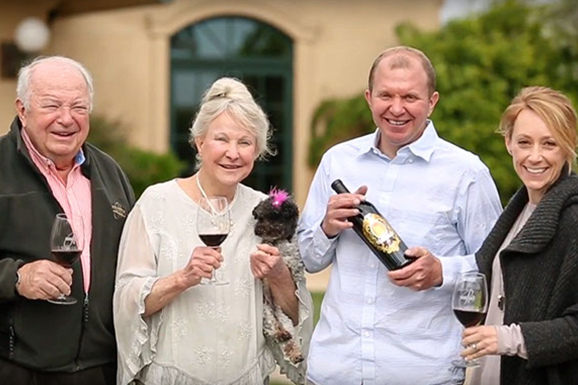 A group of people standing next to each other holding wine glasses and a bottle of wine.