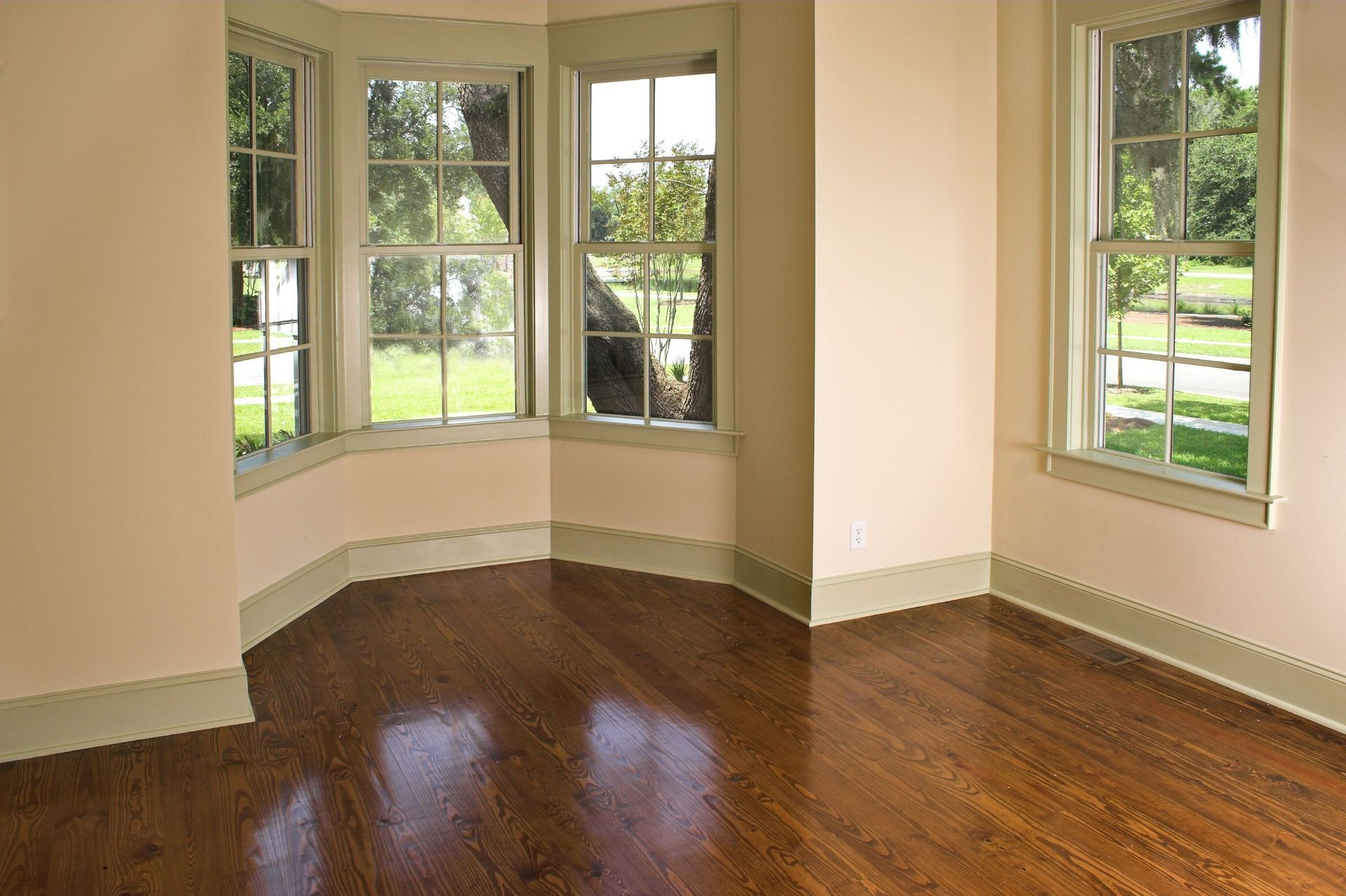 a bay window with green trim in an empty room with hardwood flooring